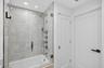 Shower enclosure featuring luxury patterned wall tile, frameless glass door, adjustable-height handheld showerhead, wall-mounted faucet controls, and 