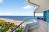 Expansive wraparound balcony featuring glass panel railings, wood look plank porcelain flooring, recessed lighting, and direct oceanfront exposure. Ad