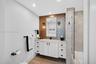 Bathroom w/ custom wall hung white vanity with matte black hardware, metallic mosaic tile accent wall, recessed lighting, and a glass-enclosed shower 