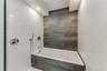 Built-in deep soaking tub featuring wood-finish tile surround, white subway tile walls, chrome shower fixtures, and recessed ceiling lighting