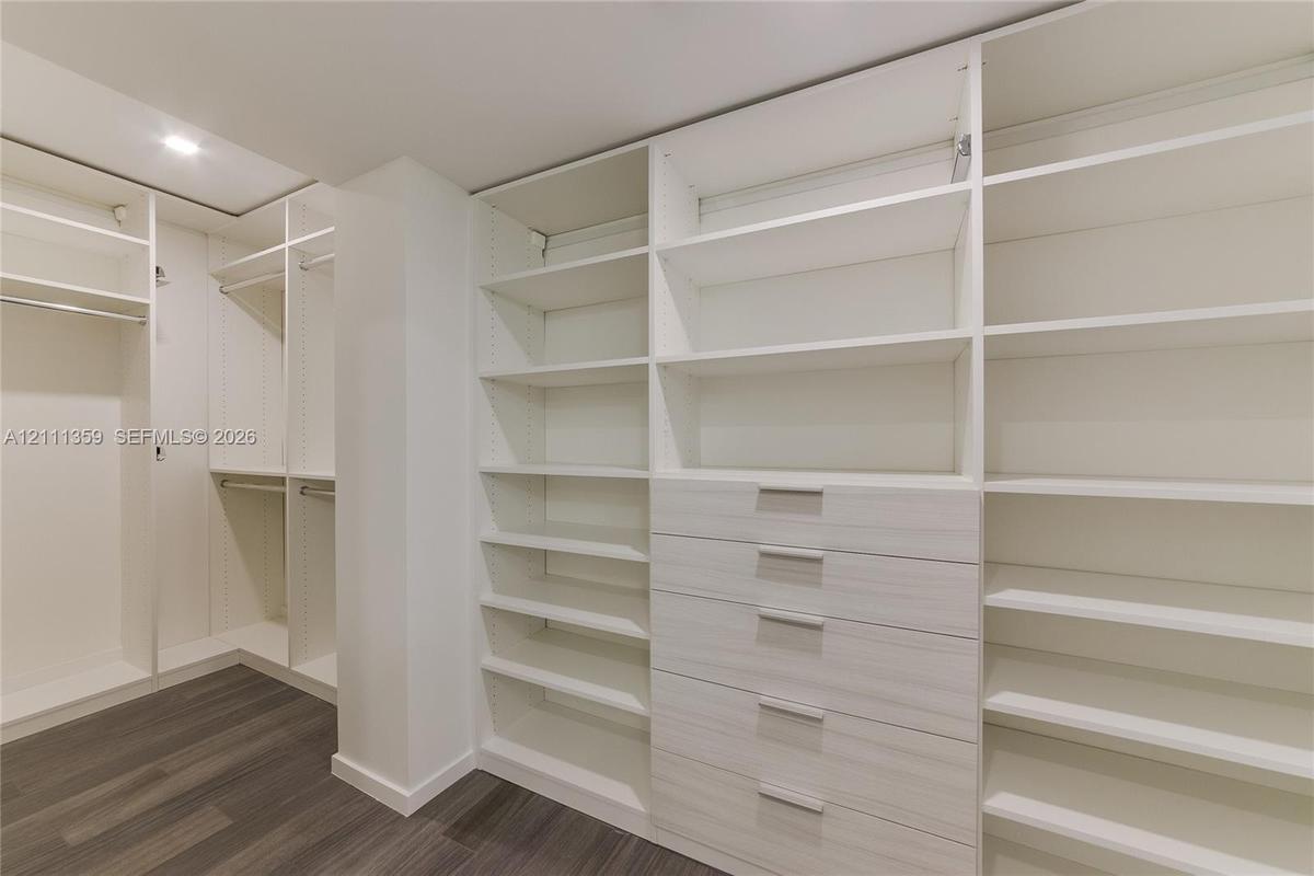 Walk-in closet featuring extensive built-in shelving, integrated wood-finish cabinetry, a bank of five drawers with metallic hardware, and dark wood-f