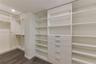 Walk-in closet featuring extensive built-in shelving, integrated wood-finish cabinetry, a bank of five drawers with metallic hardware, and dark wood-f