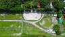 Aerial view of property featuring a sand-surfaced arena, cleared pasture land, winding paved pathways, and mature tree-lined perimeters
