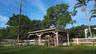 Open-air wood structure featuring a post-and-beam frame, set within a fenced area with mature trees
