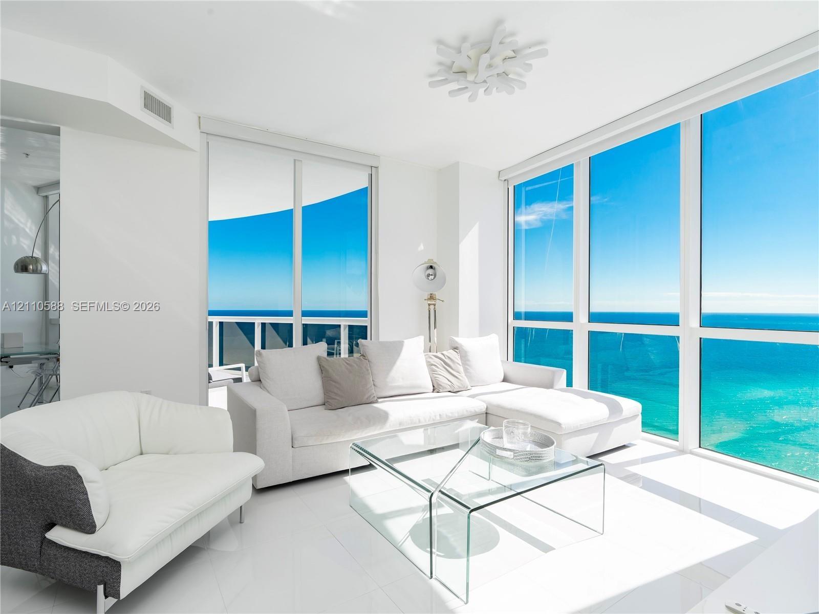 Floor-to-ceiling windows, white tile flooring, sliding glass door, white geometric ceiling fixture, and exterior balcony