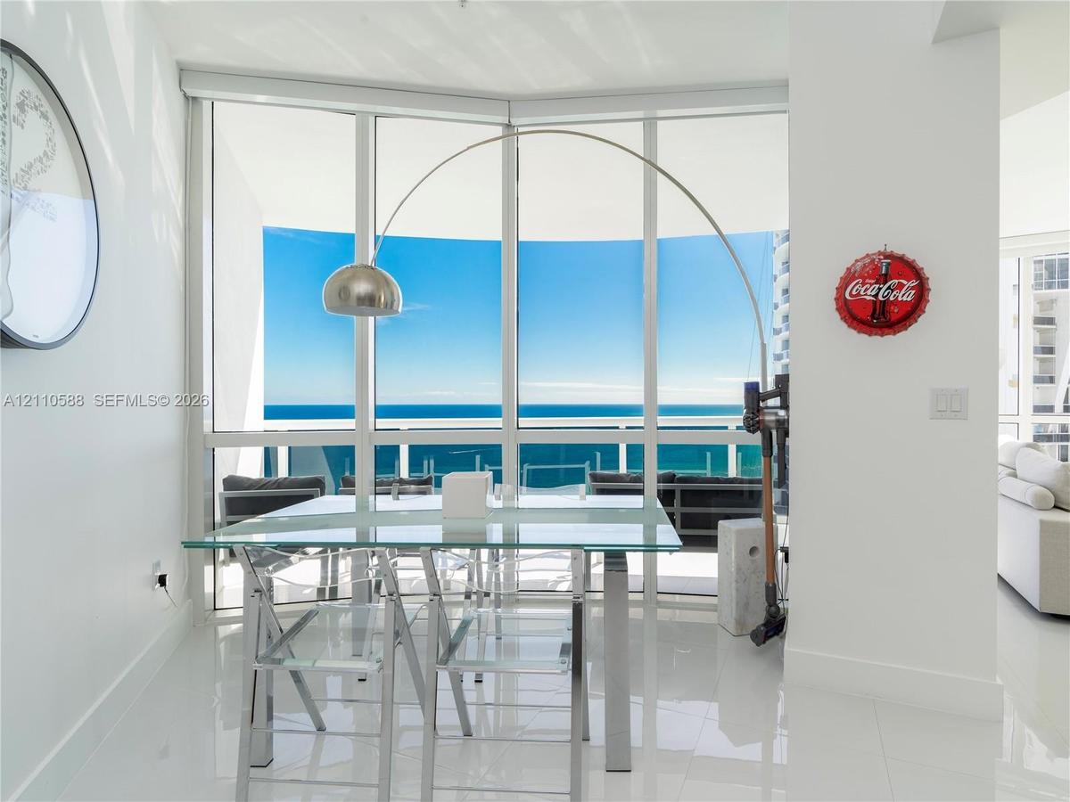 Floor-to-ceiling glass windows, polished tile flooring, and a glass-paneled balcony railing with expansive ocean exposure