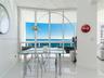 Floor-to-ceiling glass windows, polished tile flooring, and a glass-paneled balcony railing with expansive ocean exposure