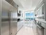 Modern galley kitchen featuring high-gloss cabinetry, stainless steel professional-grade appliances, dark stone countertops, polished tile flooring, a