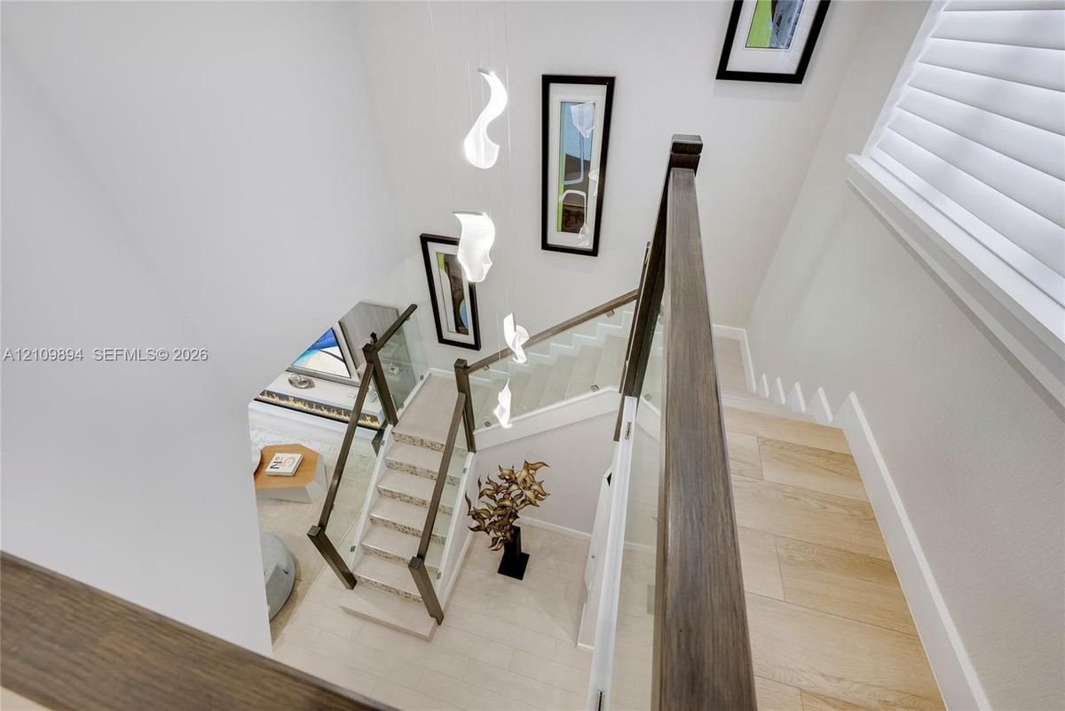 Staircase featuring wood-finish treads, glass balustrades with dark wood handrails, wood-finish flooring, white plantation shutters, and a suspended m