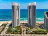 High-rise waterfront towers featuring expansive floor-to-ceiling windows, multiple hard-surface tennis courts, landscaped grounds with integrated pool