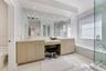 Double vanity featuring cabinetry with satin-finish hardware, integrated quartz countertops, an inset makeup station, full-width wall mirror, and a gl