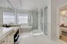 Bathroom featuring a dual-sink vanity with stone countertops, a deep soaking tub, a glass-enclosed shower, and frosted-glass sliding doors with recess