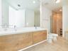 Floating dual-sink vanity with wood-finish cabinetry, expansive wall-mounted mirror, stone-tile flooring, and glass-enclosed shower