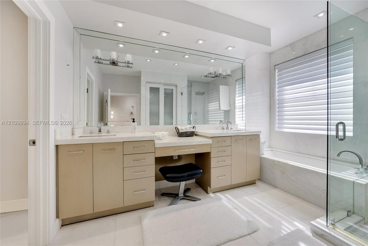 Dual vanity with integrated stone-finish countertop, recessed lighting, expansive wall-to-wall mirror, glass-enclosed shower, and a built-in soaking t
