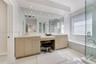 Dual vanity with integrated stone-finish countertop, recessed lighting, expansive wall-to-wall mirror, glass-enclosed shower, and a built-in soaking t