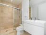 Modern wall-mounted vanity with a rectangular sink, stone-tiled walk-in shower with a glass enclosure, and large-format wall mirror