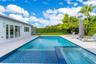 Backyard featuring a custom swimming pool with integrated spa, tile finish, expansive light-toned hardscaping, and privacy hedge