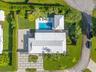 Aerial view of property featuring a metal roof, rectangular swimming pool, expansive concrete paver driveway, manicured lawn, and mature perimeter hed