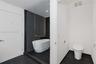 Freestanding soaking tub enclosed in a glass shower stall with dark tile surround, complemented by dark floor tiling and a white high-profile toilet