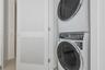 Stacked white front-loading laundry appliances enclosed within a closet featuring a white louvered door