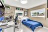 Bedroom featuring glossy tile flooring, neutral wall tones, dual horizontal windows with roller shades, built-in white shelving, and a flush-mount cir