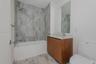 Bathroom featuring a wood-finish vanity with a white countertop, full-height wall-mounted mirror, tub with chrome fixtures, and large-format tile surr
