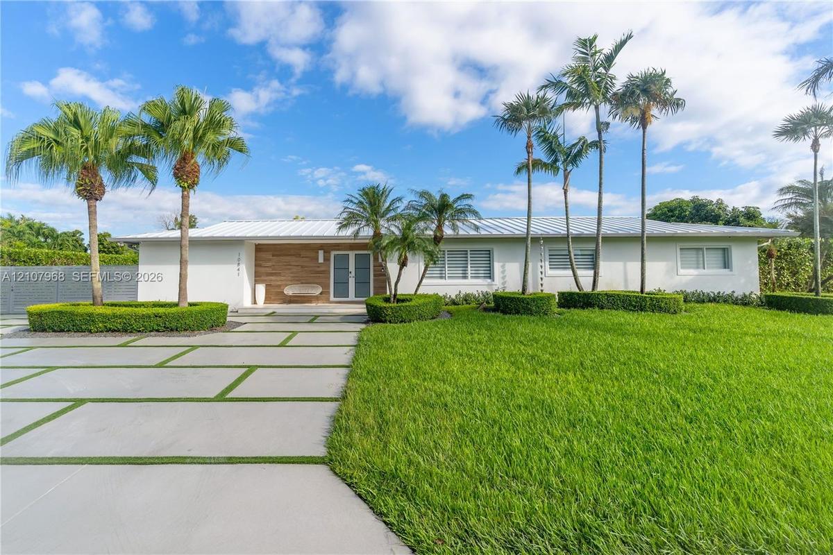 Single-story residence featuring a standing-seam metal roof, horizontal wood-panel siding, a concrete paver driveway with integrated turf, and profess