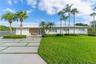 Single-story residence featuring a standing-seam metal roof, horizontal wood-panel siding, a concrete paver driveway with integrated turf, and profess