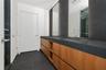 Dual-sink vanity featuring wood-finish cabinetry, dark stone countertops, tall wall-mounted mirrors, and sleek chrome fixtures with dark tile flooring