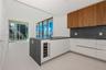 Modern kitchen featuring white flat-panel cabinetry, wood-veneer upper cabinets, integrated wine refrigerator, dark stone-finish countertops and backs