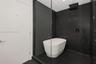 Soaking tub positioned within a glass-enclosed wet room featuring floor-to-ceiling dark-toned stone-finish tile, a rainfall showerhead, and a handheld