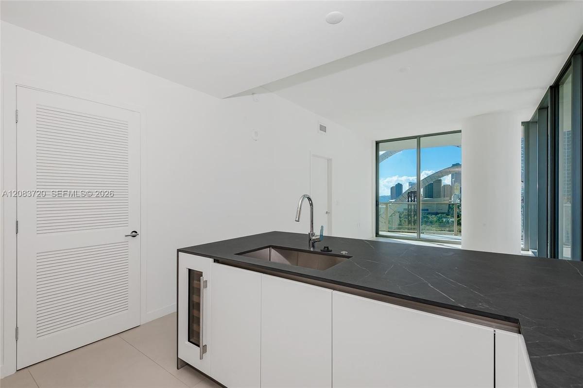Kitchen island featuring a dark stone countertop, integrated wine refrigerator, stainless steel undermount sink, and high-arc faucet, with white louve
