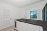 Kitchen island featuring a dark stone countertop, integrated wine refrigerator, stainless steel undermount sink, and high-arc faucet, with white louve
