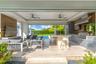 Covered outdoor living space featuring a built-in kitchen with a professional-grade stainless steel grill, stone-topped island with seating, wood-fini