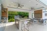 Covered outdoor kitchen and living space featuring a stone-topped island with stainless steel appliances, wood-finish wall paneling, dual ceiling fans