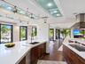 Kitchen featuring dark wood-finish cabinetry, solid-surface countertops, track lighting with glass accent panels, a stainless steel range hood, and wo