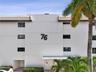 Multi-story exterior featuring a smooth stucco facade, horizontal relief detailing, dark-framed windows, a flat-tile roofline, and mature palm trees