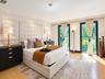 Floor-to-ceiling tufted fabric headboard, recessed ceiling lighting, and two full-length glass doors with dark frames and integrated drapery