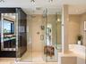 Enclosed glass shower with dual overhead rainfall fixtures, porcelain-tiled walls, built-in corner soaking tub, and vanity with an integrated vessel s
