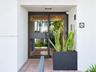 Entrance featuring a black metal-framed glass door, brick-paved walkway, recessed ceiling lighting, and a square address tile