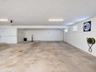 Covered parking area featuring concrete flooring, flush-mount lighting, louvered wall vents, and a mounted utility hose reel