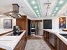 Kitchen featuring custom wood cabinetry, stainless steel appliances including a built-in double oven and range hood, white solid-surface countertops, 
