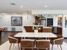 Open-concept interior featuring wood-finish cabinetry, stone-surfaced countertops, stainless steel kitchen appliances, pendant lighting, and dark wood