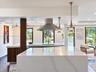 Kitchen featuring a waterfall-edge stone island, wood-finish cabinetry, stainless steel range hood, gooseneck faucet, and conical pendant lighting