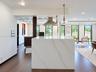 Waterfall kitchen island with stone countertop, wood-finish flooring, stainless steel range hood, pendant lighting, and dark-toned cabinetry