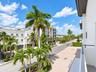Balcony featuring a metal railing, overlooking a paved street with mature palm trees and landscaped greenery