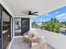 Covered terrace featuring large-format tile flooring, a matte black ceiling fan with integrated lighting, and a black metal railing overlooking the wa