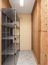 Storage space featuring metal wire shelving, plywood-paneled walls with wire grid overlays, and concrete flooring