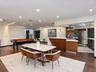 Open-concept kitchen featuring flat-panel wood cabinetry, integrated stainless steel appliances, a stainless steel range hood, and a kitchen island wi