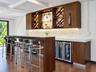 Custom wet bar featuring wood-finish cabinetry, built-in wine storage, integrated under-cabinet lighting, and a glass-topped counter